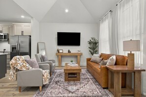 A modern living room with a sofa, armchair, coffee table, and a TV mounted on the wall.