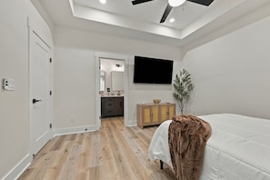 A bedroom with a bed, a television, a plant, and a bathroom visible through an open door.