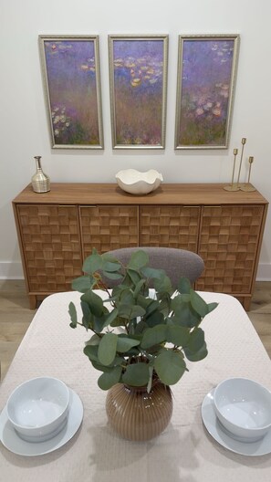 A dining table with a vase of green leaves, two white bowls, and a wooden cabinet with a woven pattern.