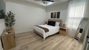 A bedroom with a bed, bedside tables, a ceiling fan, a window with curtains, and a mirror.