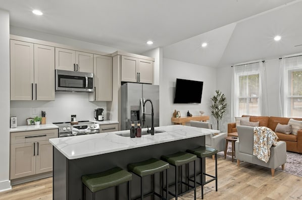 A modern kitchen with a central island, bar stools, and a flat-screen TV mounted on the wall.