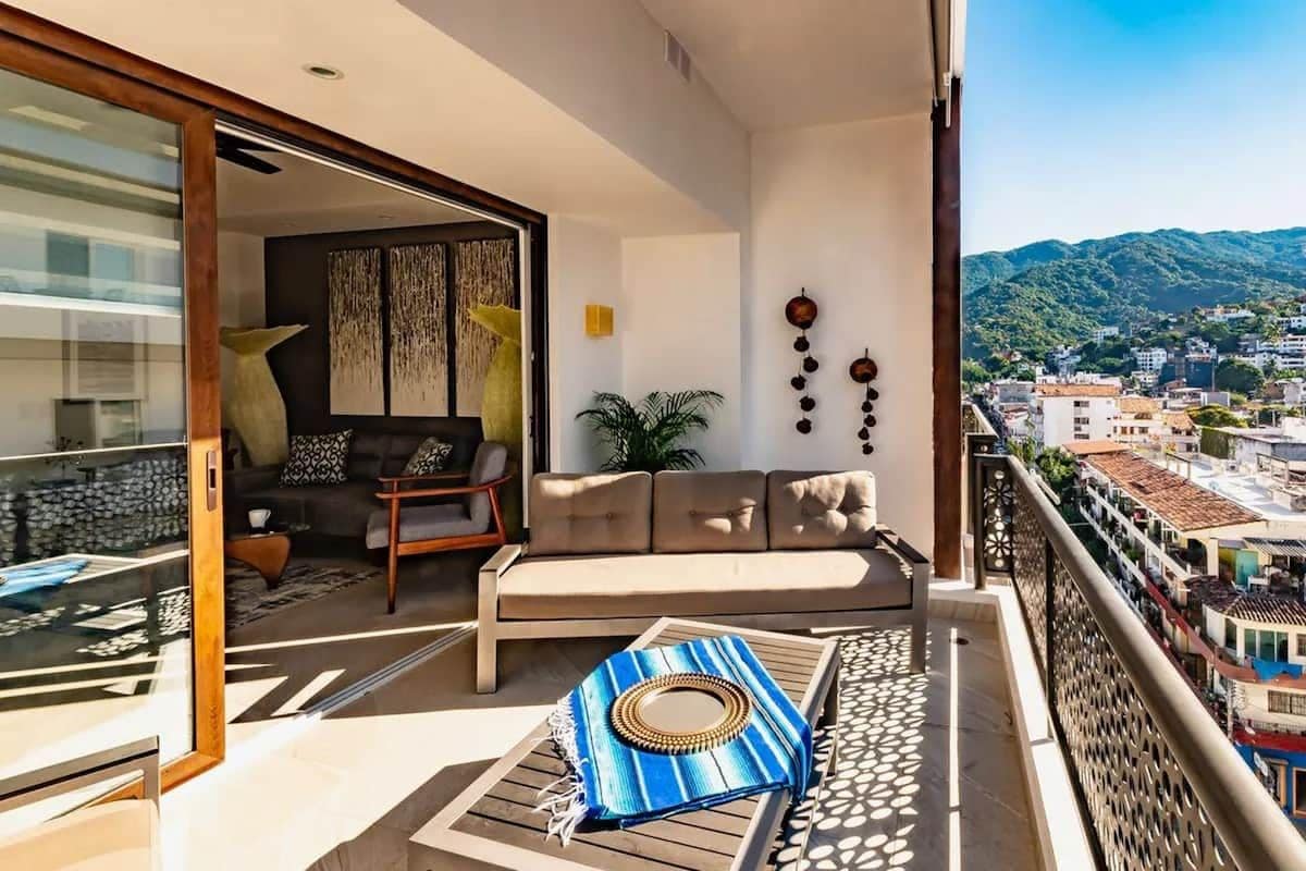 A balcony with a sofa, a patterned rug, and a view of a cityscape.