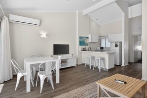 A modern living space with a dining area, kitchen, and a TV. - Coastal Comfort 1 Bed Apartment (Noosa Heads)
