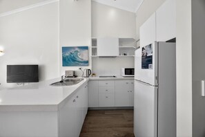 A modern kitchen with white cabinetry, a built-in microwave, and a kettle. - Coastal Comfort 1 Bed Apartment (Noosa Heads)