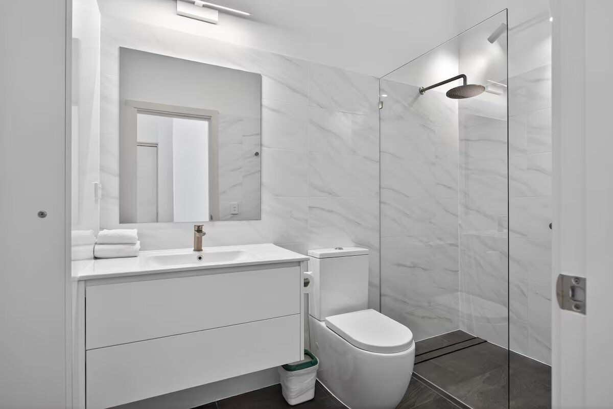 A modern bathroom with a white vanity, a toilet, and a glass-enclosed shower area.