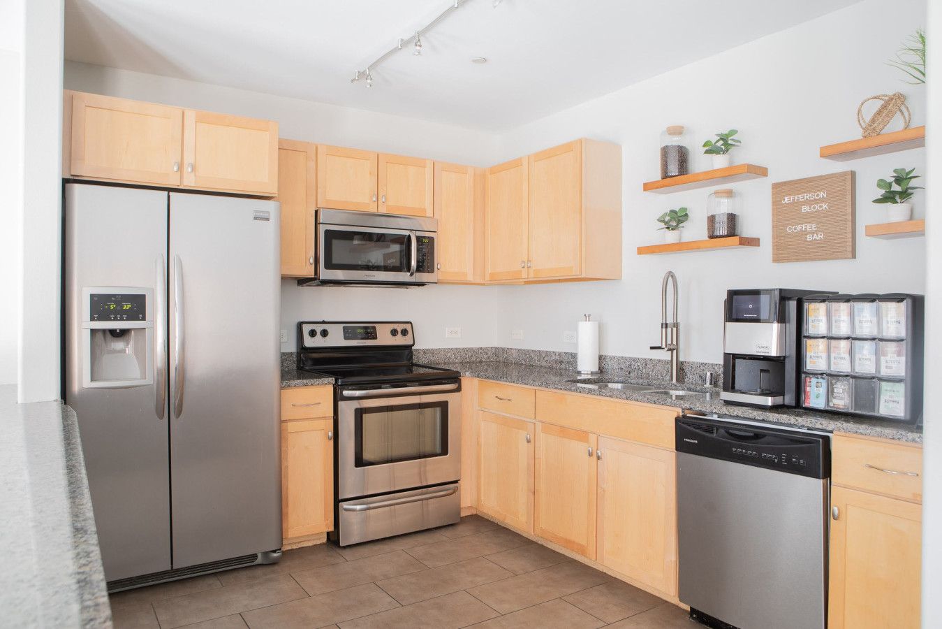 A modern kitchen with stainless steel appliances, wooden cabinets, and a coffee station.