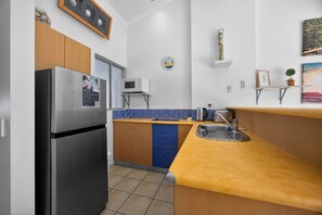 A compact kitchen with a refrigerator, microwave, and sink. - Couples Budget Stay on Noosa Parade! (Noosa Heads)
