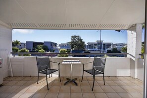 Varanda coberta com duas cadeiras e uma mesa, com vista para uma área residencial com edifícios modernos e céu claro.