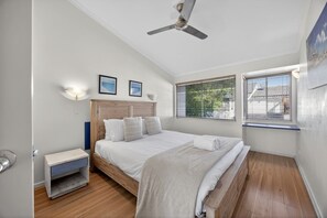 A bedroom with a bed, a nightstand, a ceiling fan, and two windows with blinds. - Couples Budget Stay on Noosa Parade! (Noosa Heads)