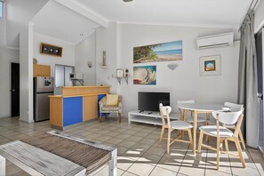 A modern living room with a kitchen area, a TV, and a dining set. - Couples Budget Stay on Noosa Parade! (Noosa Heads)