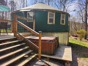 A wooden deck leading to a green yurt with a hot tub, surrounded by trees.