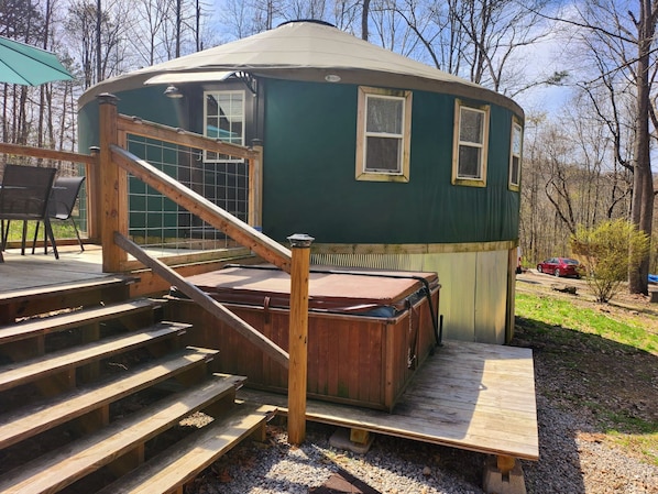 A wooden deck leading to a green yurt with a hot tub, surrounded by trees.