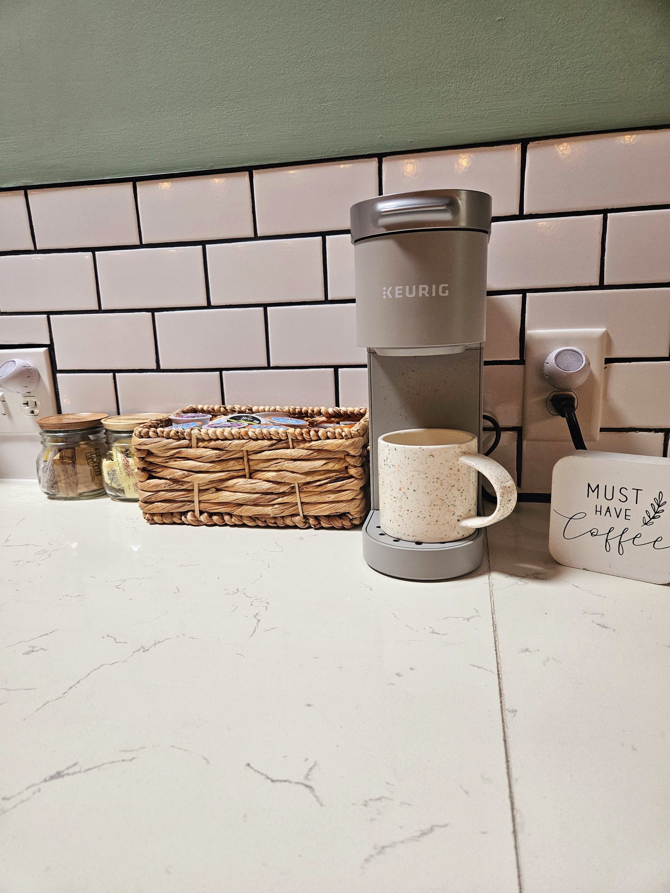 A kitchen counter with a Keurig coffee maker, a mug, jars, and a basket.