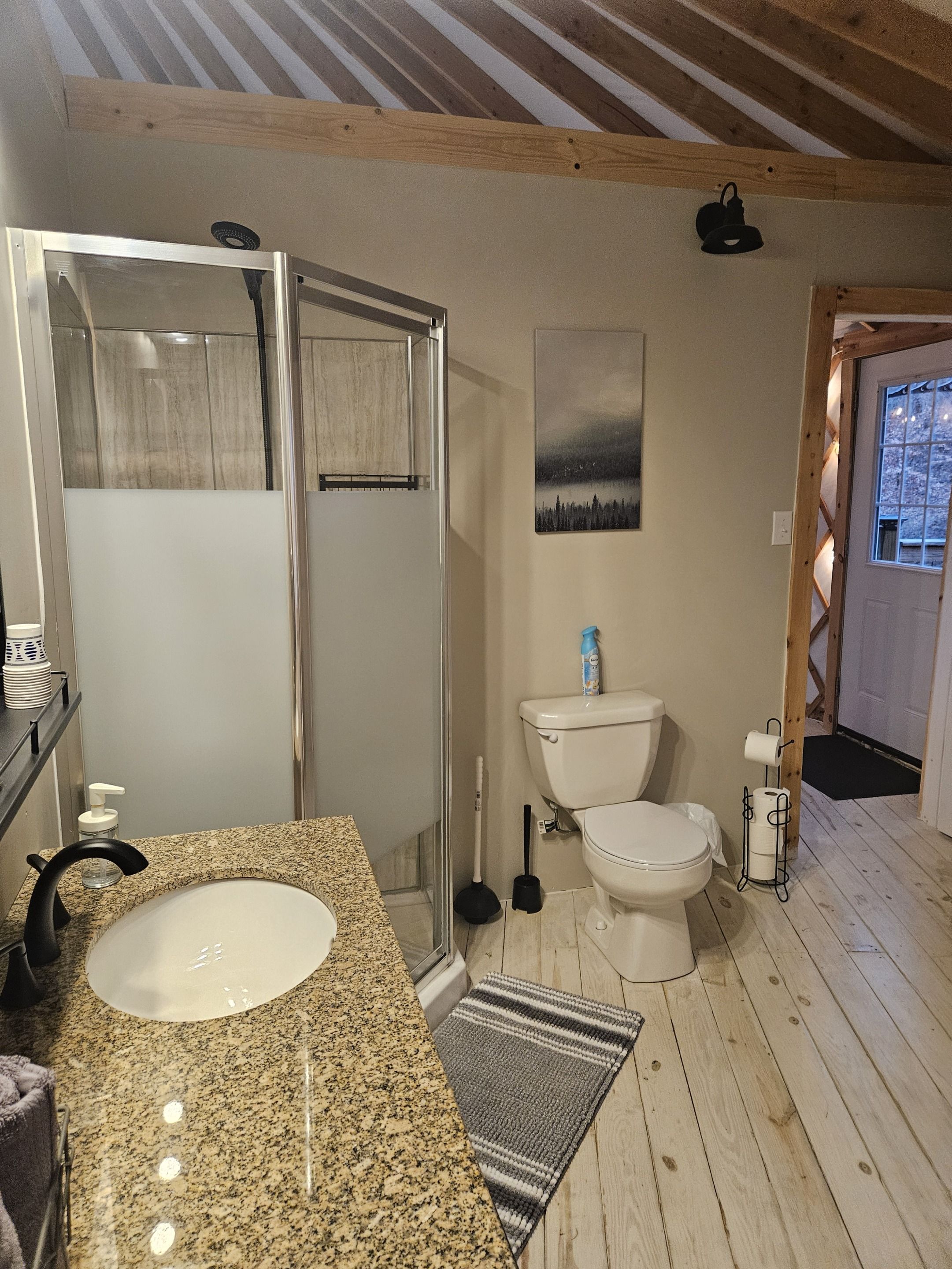 A bathroom with a granite countertop, a toilet, a shower with a glass door, and a wooden floor.