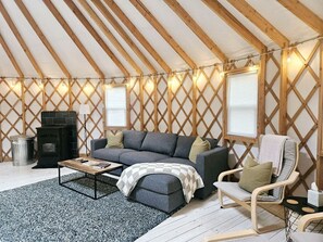 Una habitación acogedora con techo de madera, un sofá, una silla, una mesita y una chimenea.