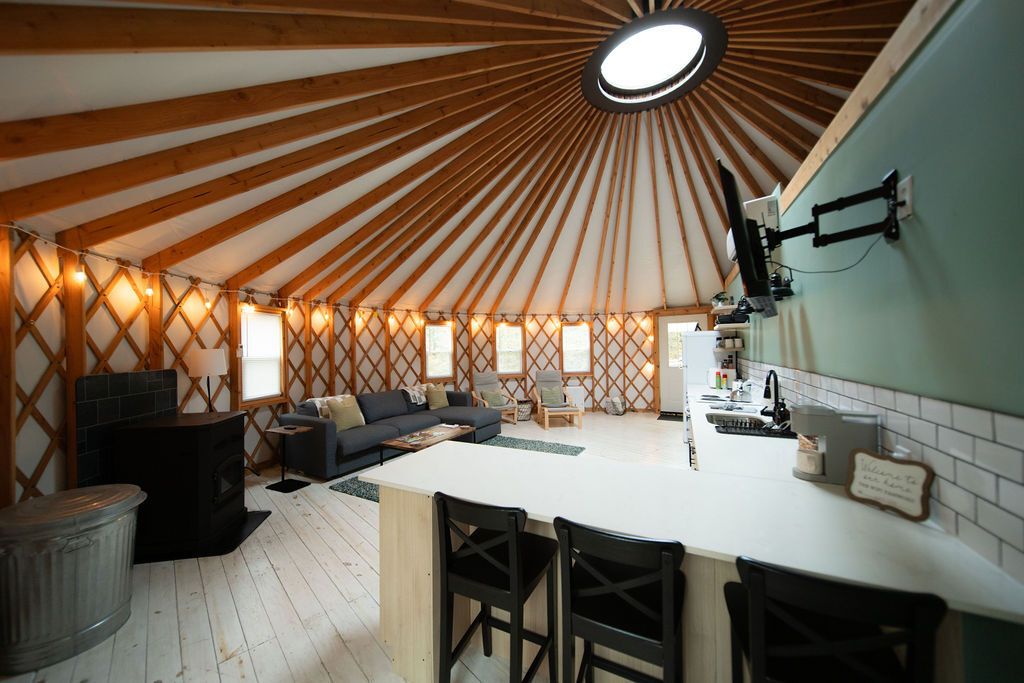 Interior de una yurta con una zona de estar central, una cocina con encimera blanca y estructura de techo de madera.