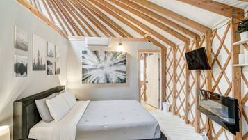 Un dormitorio con una cama, un televisor montado y una pared con cuadros.