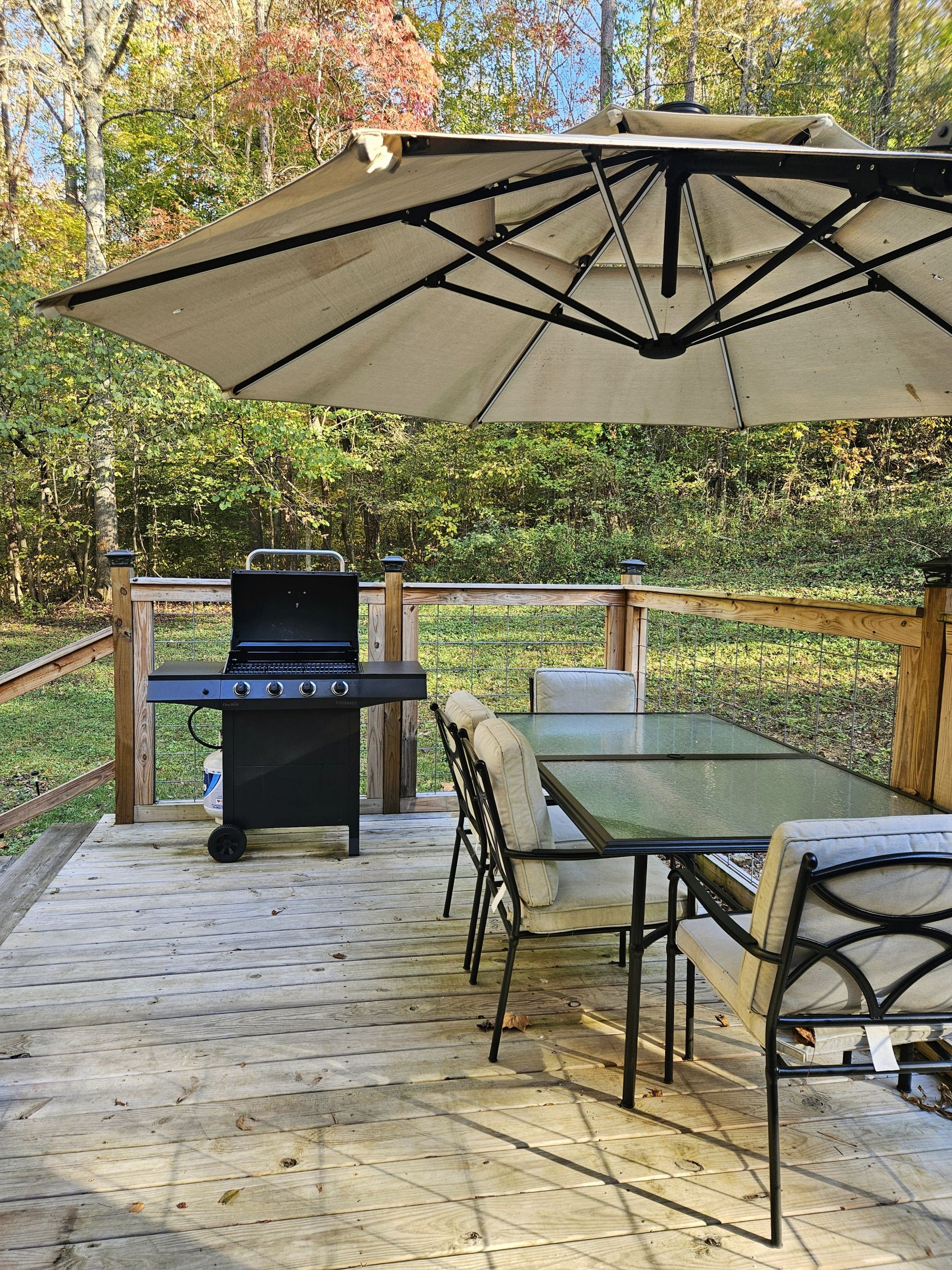 A wooden deck with a grill, table, chairs, and a canopy.