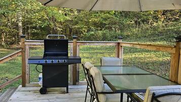 A wooden deck with a grill, table, chairs, and a canopy.