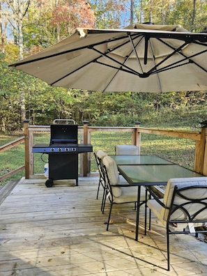 A wooden deck with a grill, table, chairs, and a canopy.
