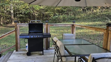 An outdoor deck with a grill, a table, and chairs, surrounded by a wooden deck and a fence.