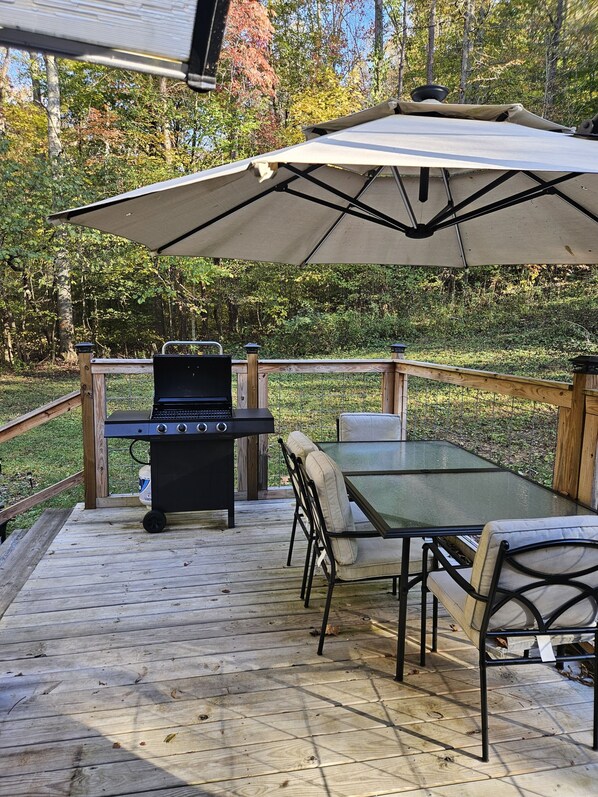 An outdoor deck with a grill, a table, and chairs, surrounded by a wooden deck and a fence.