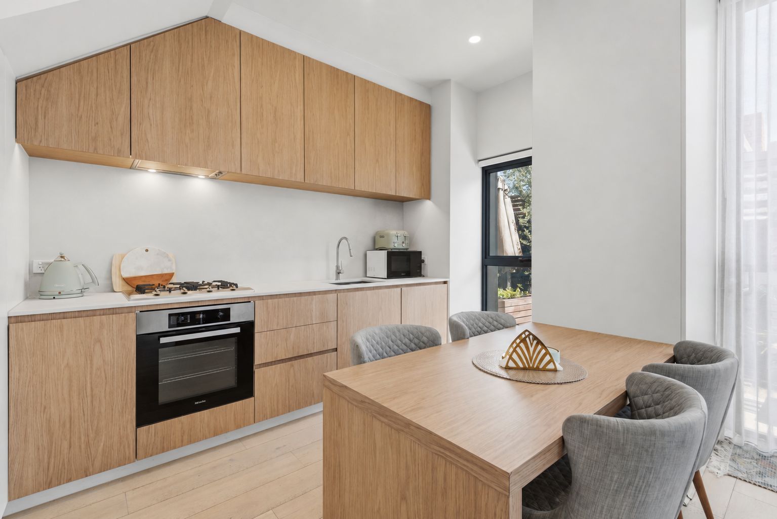 A modern kitchen with wooden cabinets, a built-in oven, and a dining area with a table and chairs.