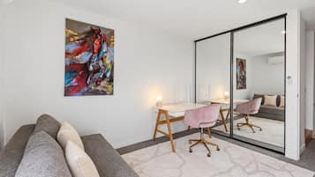 A modern room with a white desk, a pink chair, a large mirror, and a sofa with multiple cushions.