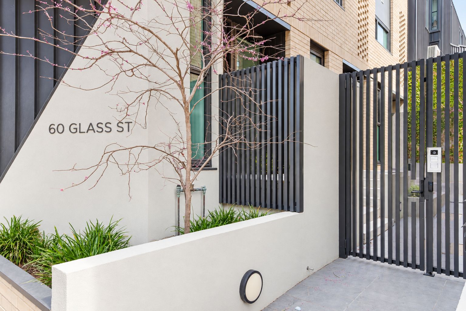 A modern building with a gated entrance, a tree with pink flowers, and a sign reading '60 GLASS ST'.