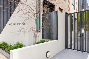 A modern building with a gated entrance, a tree with pink flowers, and a sign reading '60 GLASS ST'. - Richmond Lumiere by Ready Set Stay (Richmond)