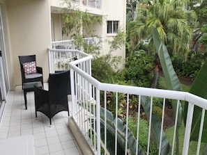 Ein Balkon mit weißen Geländern, zwei Korbstühlen und einem kleinen Tisch.