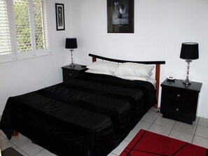 Ein Schlafzimmer mit einem schwarzen Bett, weißen Kissen, einem schwarzen Nachttisch mit Lampe und einem roten Teppich.