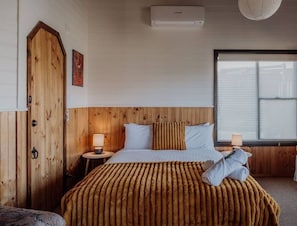 A hotel room with a wooden headboard, a bed with a striped blanket, two bedside lamps, and a window with blinds.