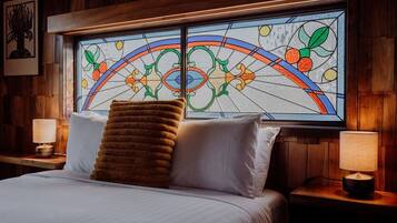 A hotel room with a bed, two bedside lamps, a large stained glass window, and a wooden headboard.