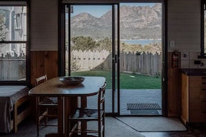 A room with a wooden table and chairs, a sliding glass door leading to a backyard with a wooden fence and mountains in the background.