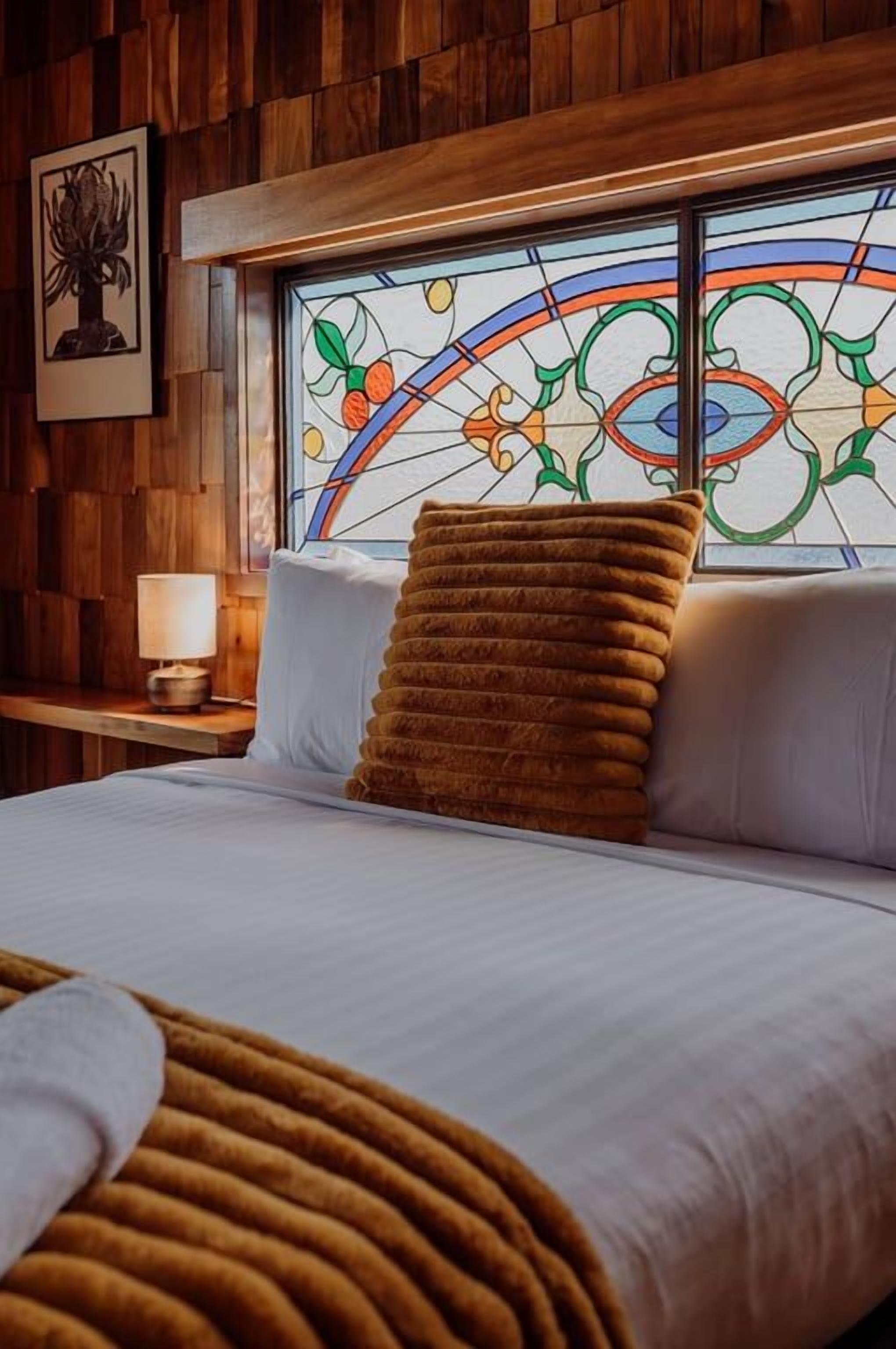 A bedroom with a bed, a window with a stained glass design, and wooden paneling on the walls.