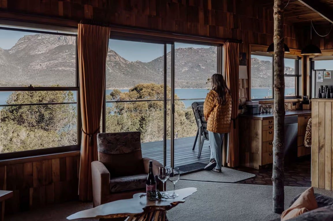 A room with large windows overlooking a mountainous landscape, a wooden interior, and a bar area.