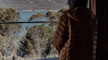 A person standing on a balcony overlooking a mountainous landscape and a body of water.