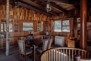 A wooden interior with a dining area, a fireplace, and a view through a window.