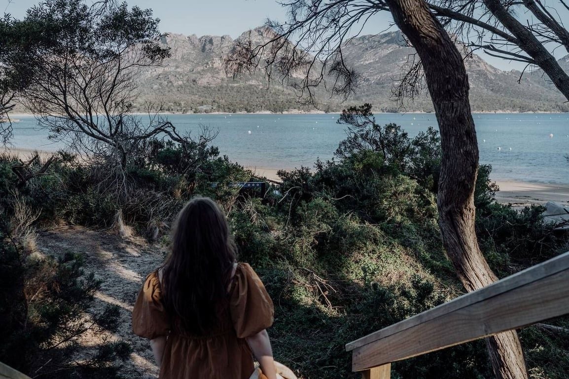 A person standing on a wooden deck overlooking a beach with a mountainous backdrop.