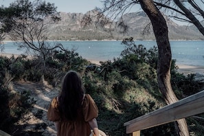 A person standing on a wooden deck overlooking a beach with a mountainous backdrop.