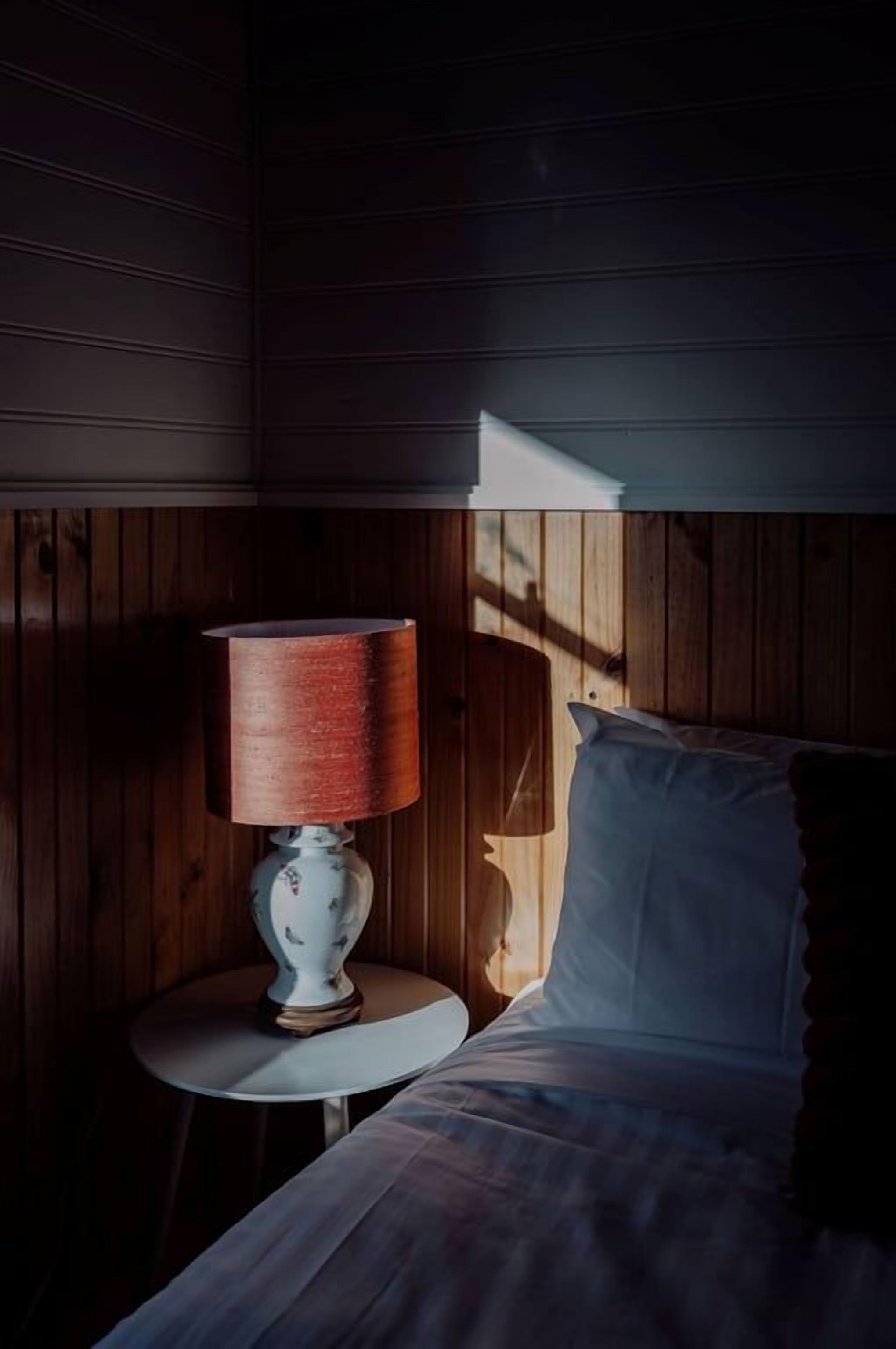 Una habitación con una cama, una mesita de noche con una lámpara y paredes de madera.
