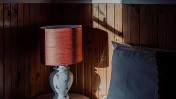 Una habitación con una cama, una mesita de noche con una lámpara y paredes de madera.