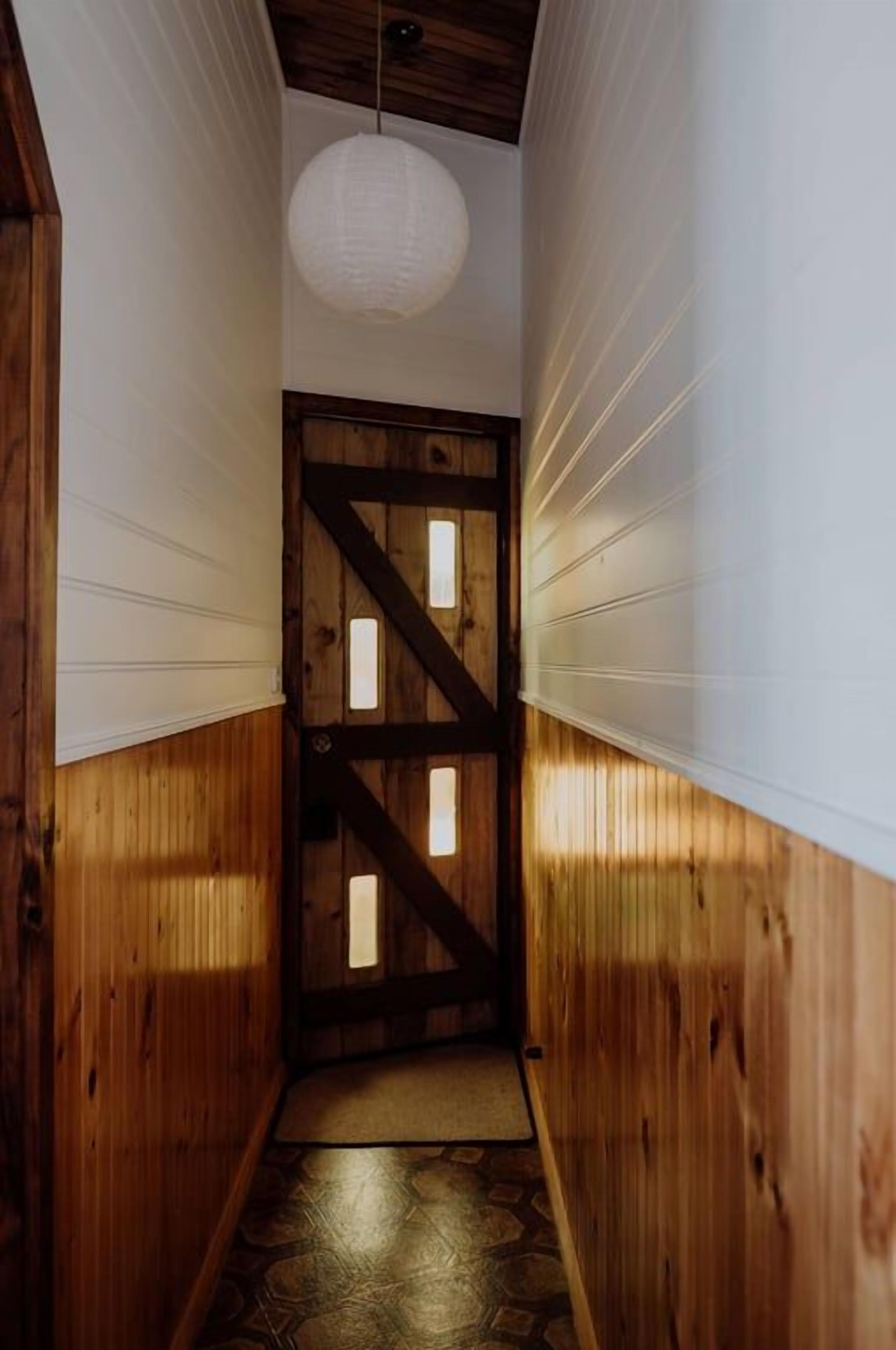 Un couloir étroit aux murs en bois et une porte en bois ornée de motifs en forme de croix.