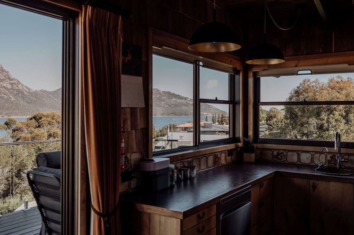 A kitchen with a view of a lake and mountains, wooden cabinets, a bar area, and a window with curtains.