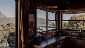 A kitchen with a view of a lake and mountains, wooden cabinets, a bar area, and a window with curtains.