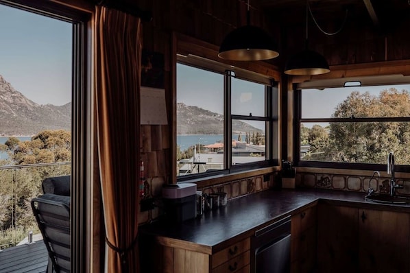 A kitchen with a view of a lake and mountains, wooden cabinets, a bar area, and a window with curtains.