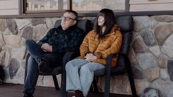 Two people sitting on a bench outside a building with stone walls and a window.