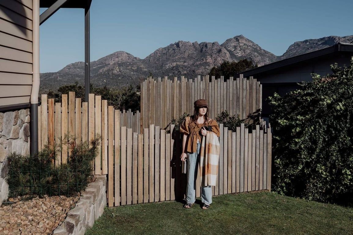 A person standing in a backyard with a wooden fence and mountains in the background.