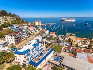 Une ville côtière dotée d’un port de plaisance, de bâtiments aux toits bleus et, au loin, d’un grand navire de croisière.